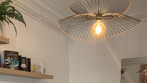 Een slaapkamer met een bed, nachtkastje, lamp, plank met boeken en een hangende lamp.