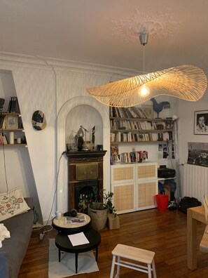 Ein gemütliches Wohnzimmer mit Kamin, Bücherregal, rundem Tisch und einer Pendelleuchte.