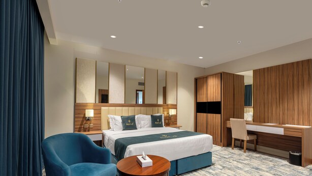 A hotel room with a bed, a desk, a chair, a small table, and a large mirror. - Aluya Al Marwa Hotel (Jeddah)