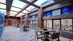 A modern interior with a high ceiling, large windows, and a dining area with tables and chairs. - Aluya Al Marwa Hotel (Jeddah)