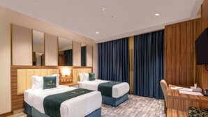 A hotel room with two beds, a desk, a chair, a flat-screen TV, and a large mirror. - Aluya Al Marwa Hotel (Jeddah)