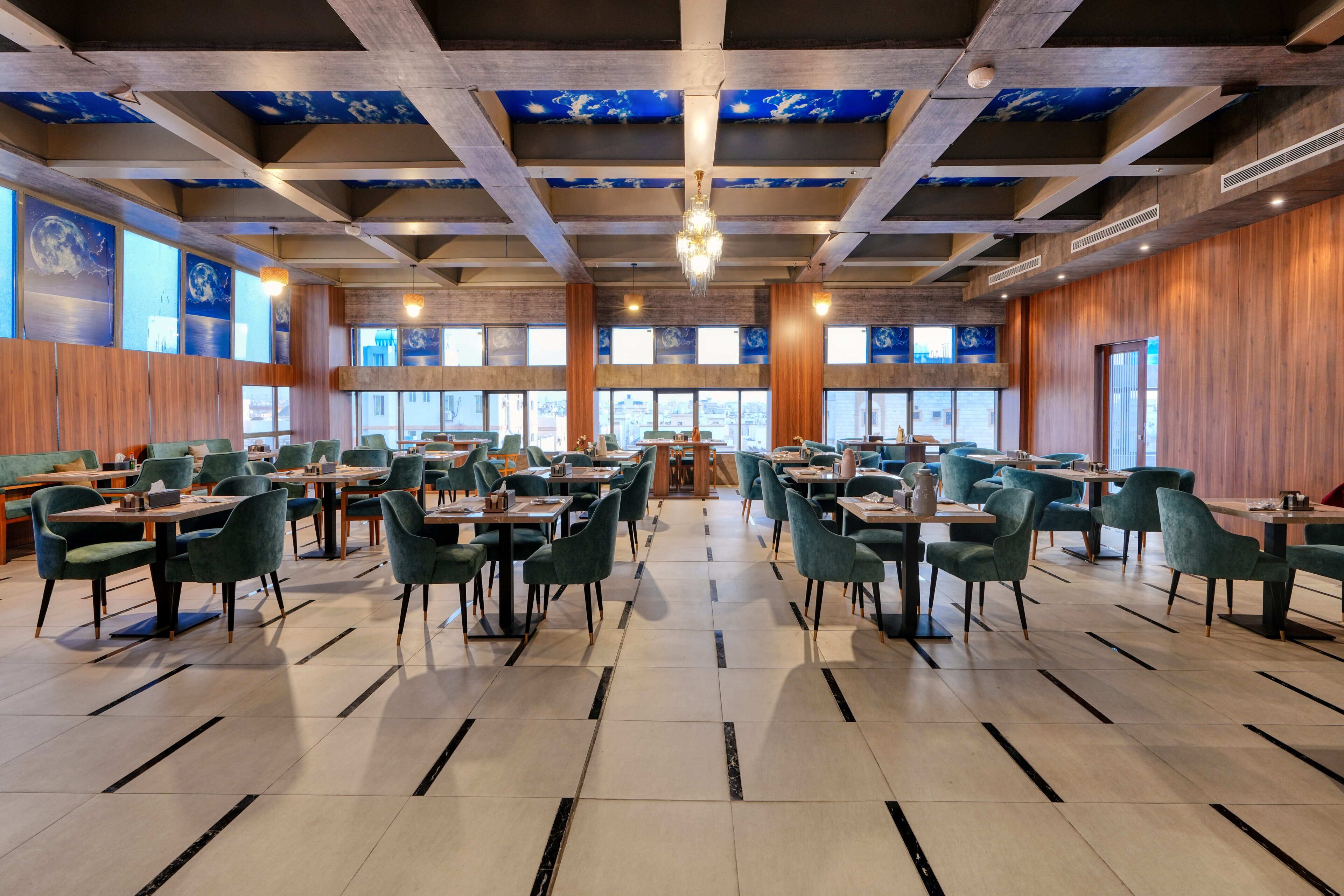 A spacious dining area with multiple tables and chairs, large windows, and a high ceiling with exposed beams.