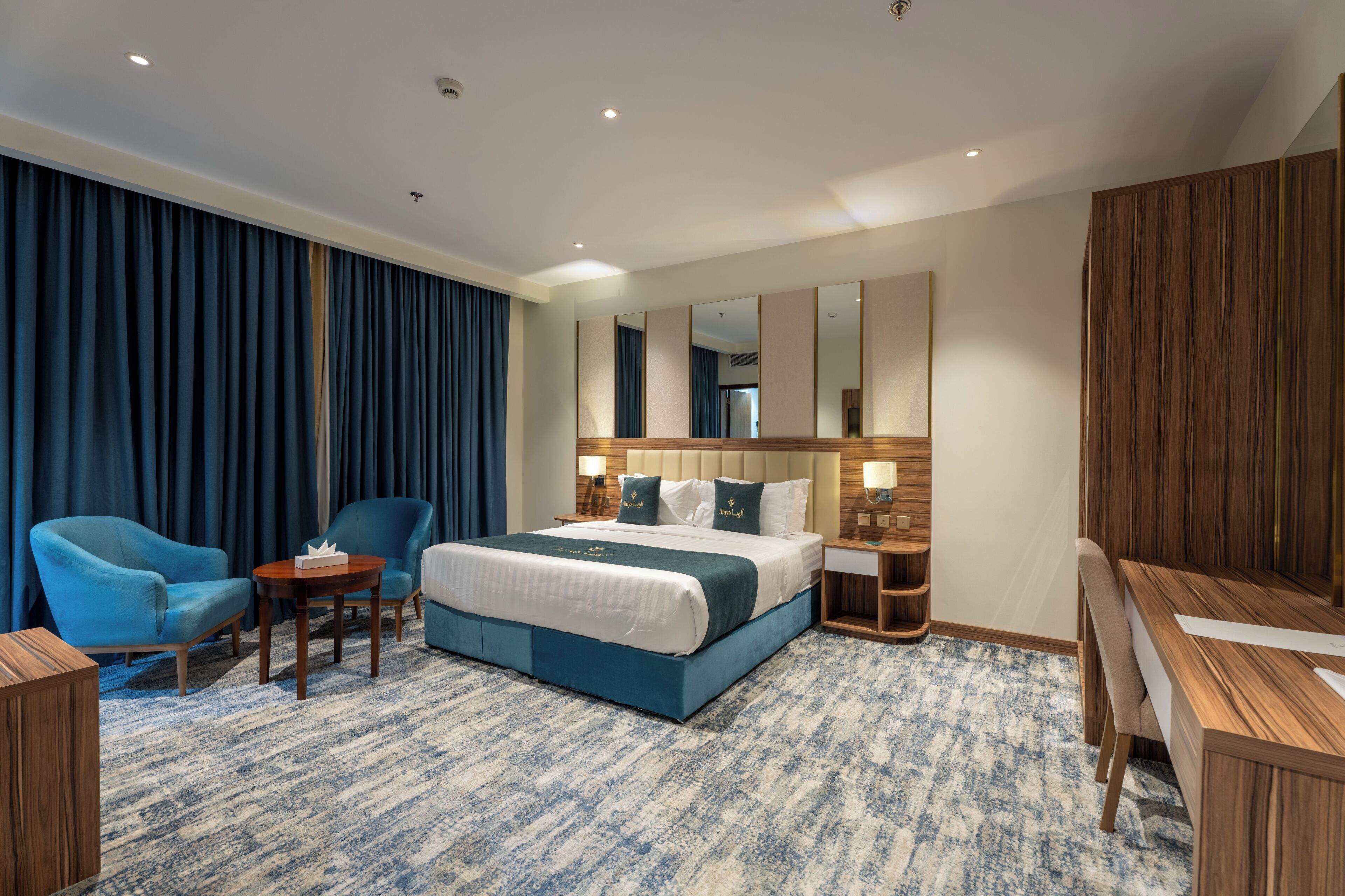 Una habitación de hotel con una cama grande, dos sillones, un escritorio y un armario.