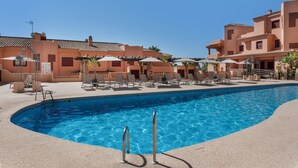 A swimming pool with lounge chairs and umbrellas, surrounded by buildings with terracotta roofs.