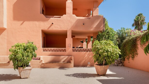 A multi-story building with balconies, potted plants, and a clear sky.