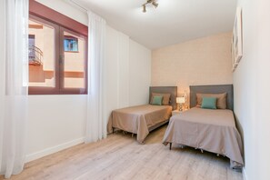 A hotel room with two beds, a window with curtains, a wooden floor, and a wall-mounted lamp. - Apartment 'Altea Marbella' with Shared Pool, Wi-Fi and Air Conditioning (Benahavís)