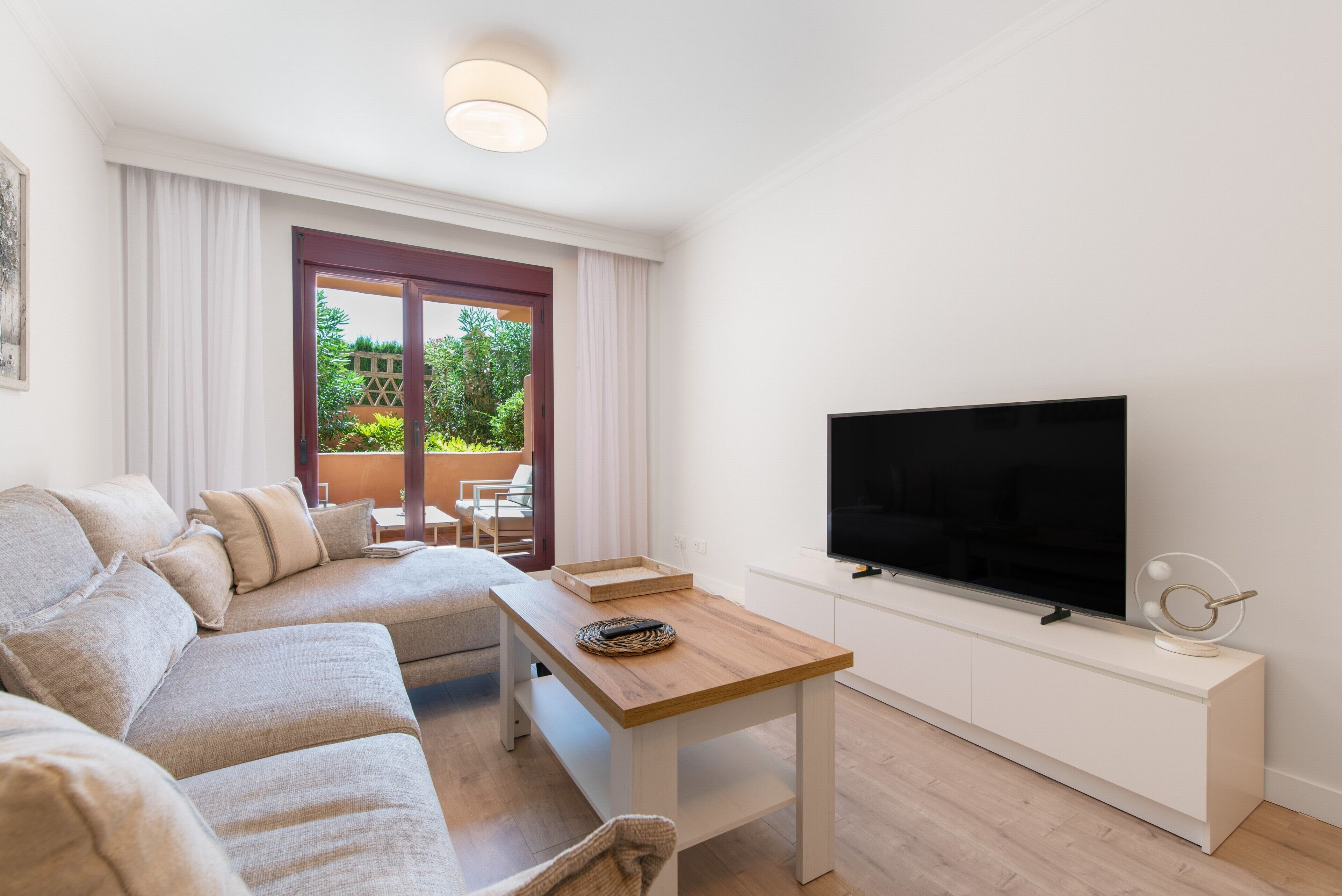 Ein modernes Wohnzimmer mit einer Couch, einem Holztisch, einem Flachbildfernseher und einem Balkon mit Pflanzen.