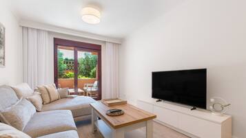 Ein modernes Wohnzimmer mit einer Couch, einem Holztisch, einem Flachbildfernseher und einem Balkon mit Pflanzen.