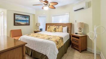 A bedroom with a bed, a desk, a chair, a ceiling fan, and a painting on the wall.