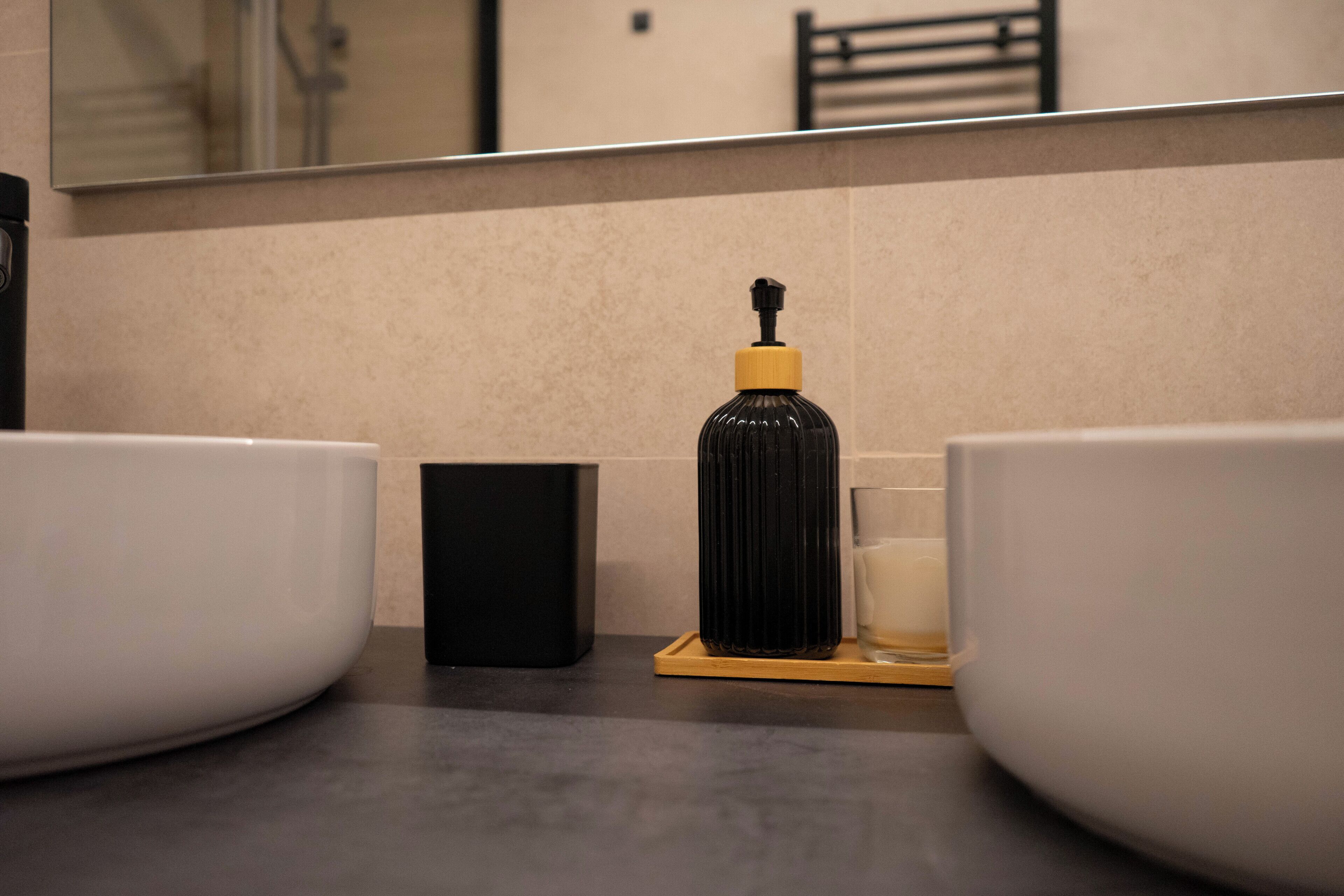 Une salle de bain avec deux lavabos blancs, un distributeur de savon noir et une petite boîte noire posée sur le comptoir.
