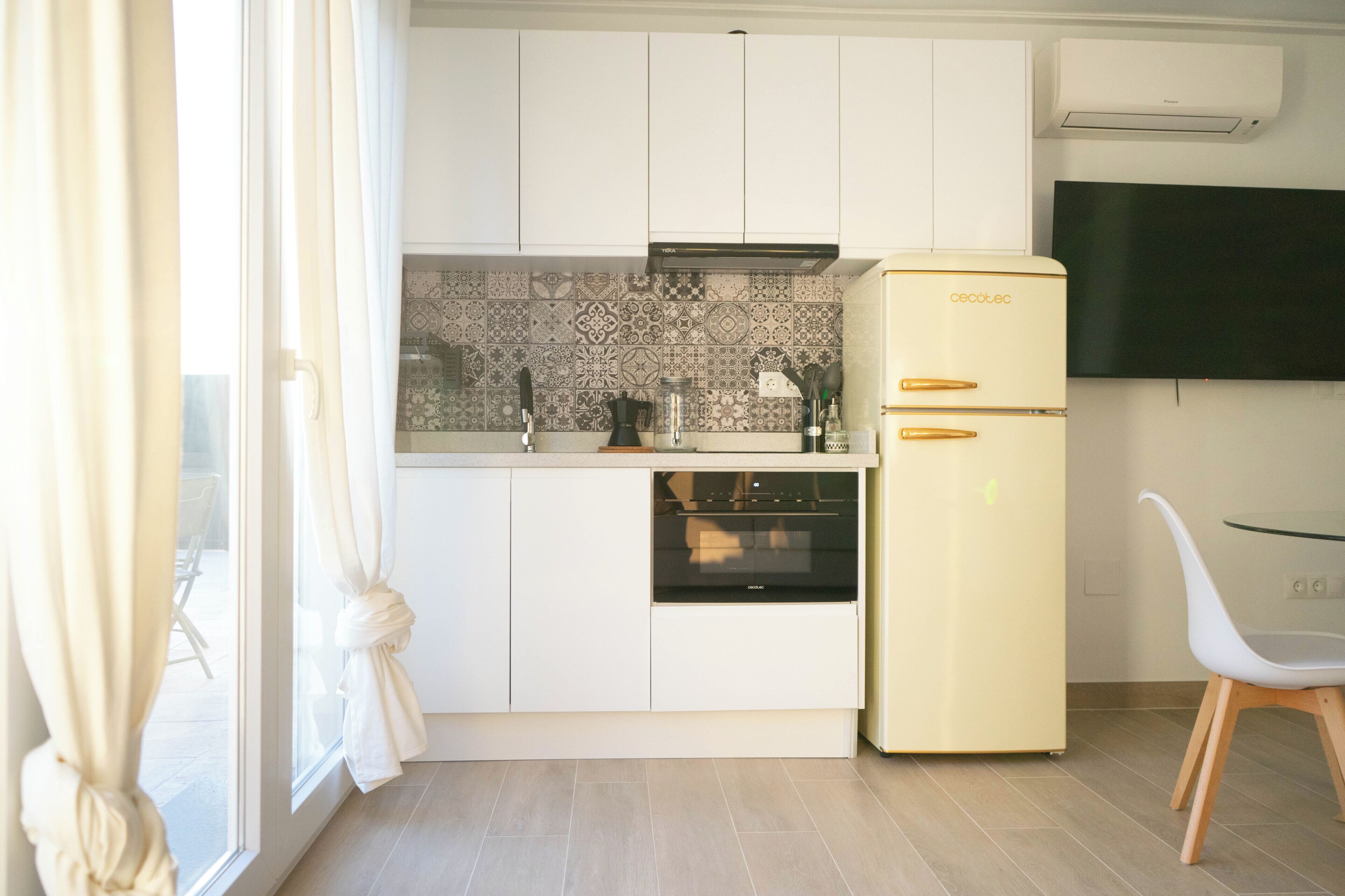 Una cocina compacta con armarios blancos, horno integrado y refrigerador amarillo.