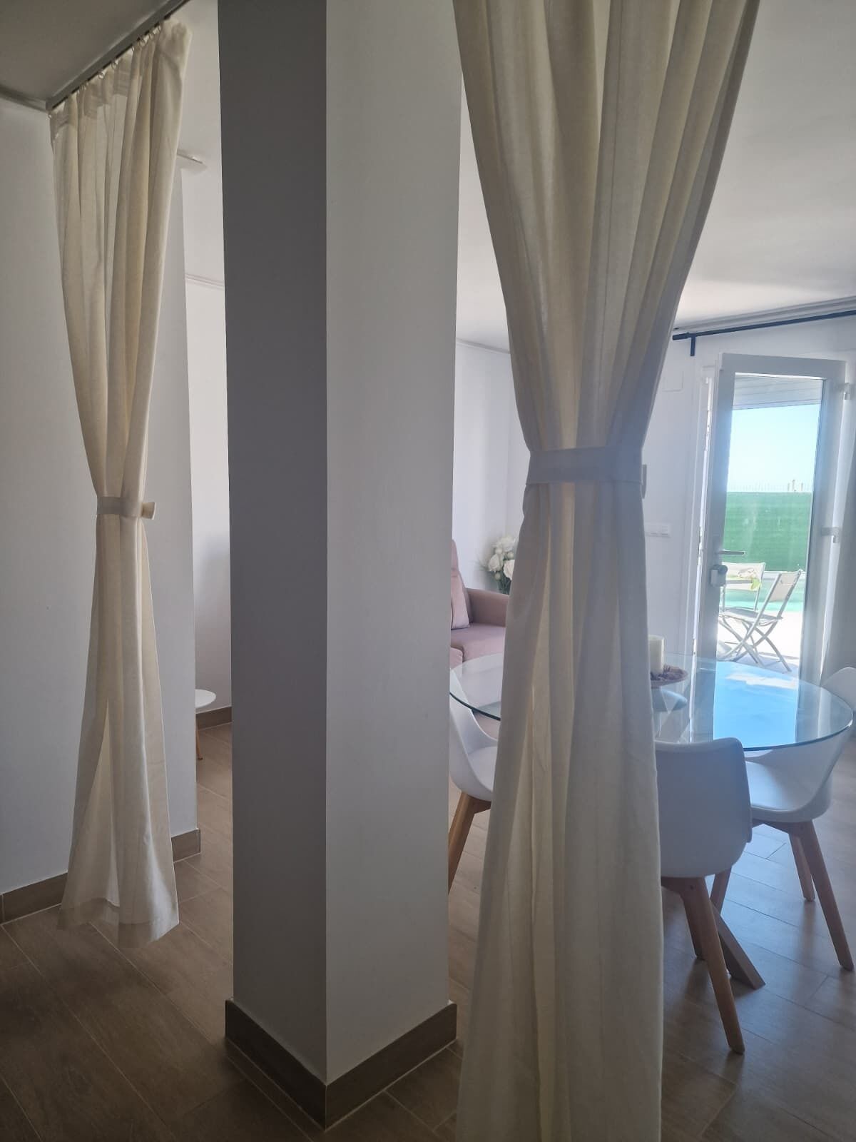Una sala de estar moderna con una mesa y sillas de vidrio, un sofá blanco y vistas a un balcón.