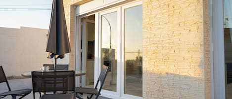 An outdoor patio with a table and chairs, a large umbrella, and a sliding glass door leading to a covered area.