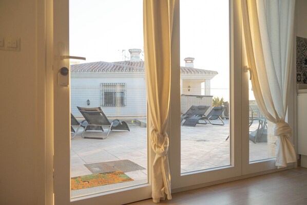 A room with a sliding glass door leading to an outdoor area with lounge chairs and a tiled patio.