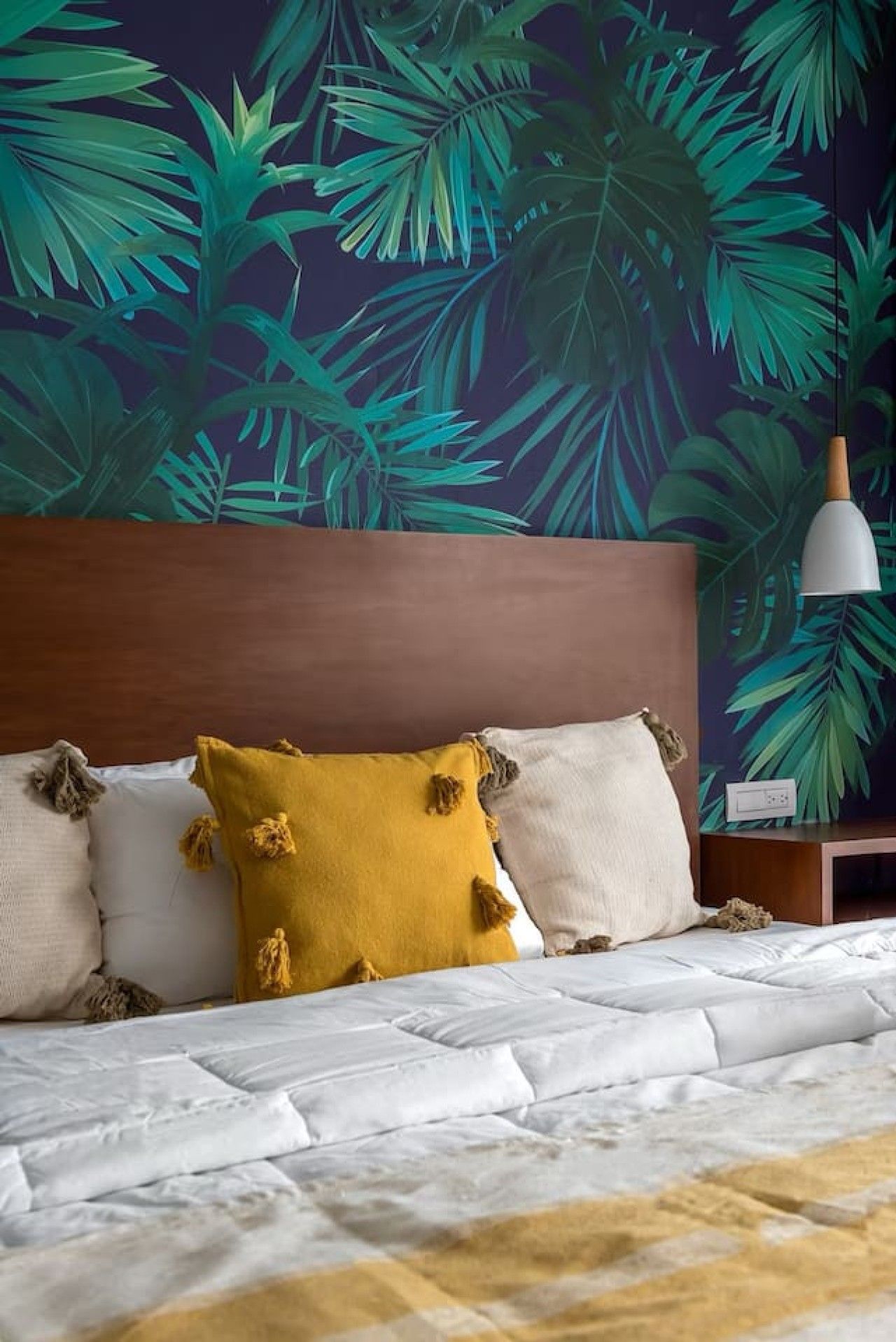 Una cama con ropa blanca, un cojín amarillo mostaza y una cabecera de madera.