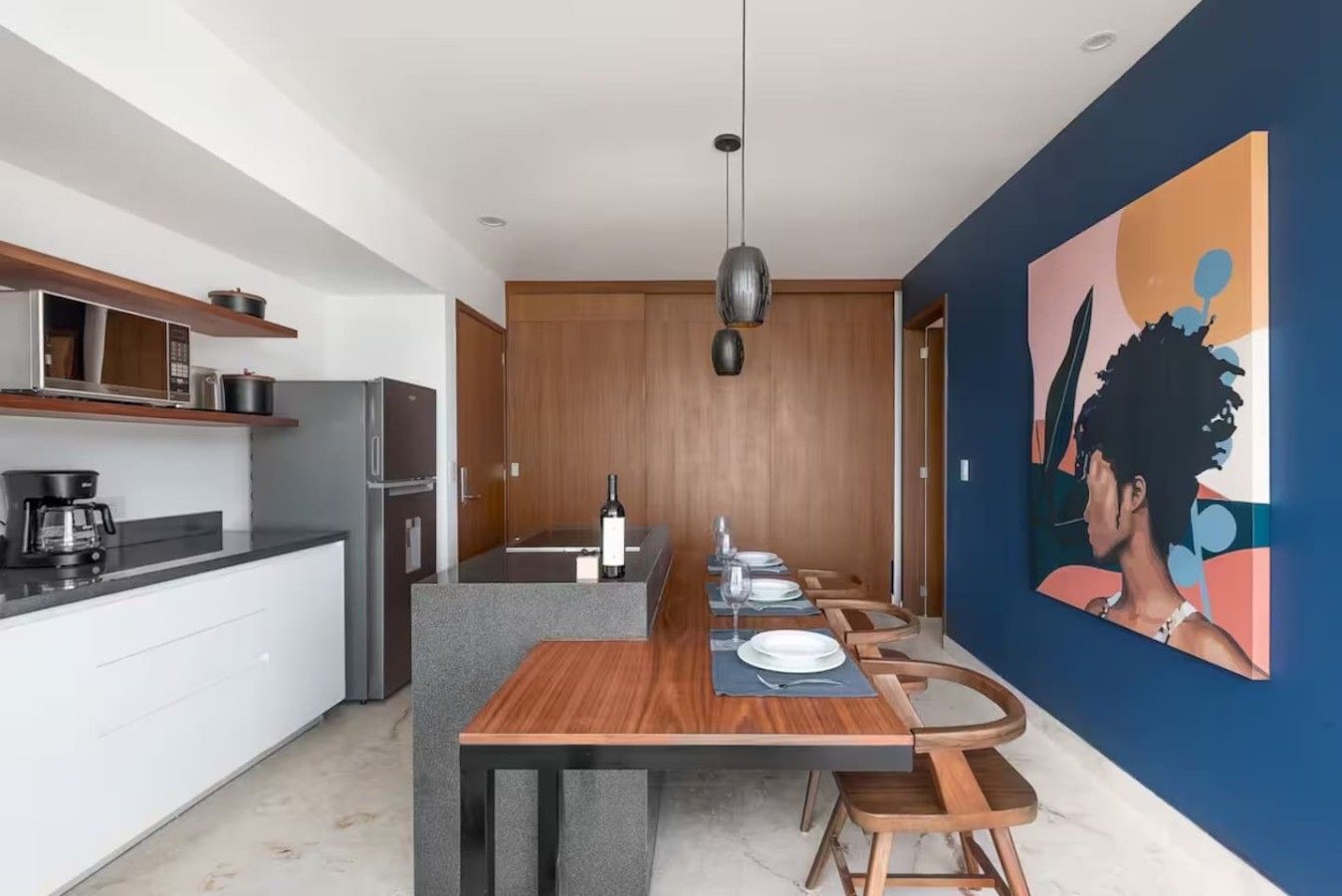 Een moderne keuken met een eethoek, een koffieapparaat, een koelkast en een schilderij aan de wand.