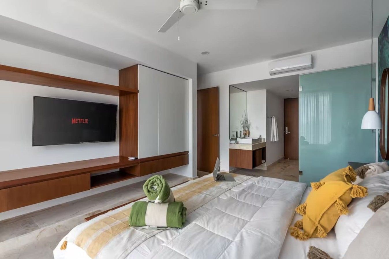 Quarto de hotel moderno com cama, televisão, escrivaninha e banheiro visível por uma porta aberta.