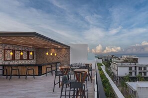 A rooftop terrace with a bar area, seating arrangements, and a view of the cityscape. - Stilvolles Apartment mit Balkon an der Quinta (Playa del Carmen)