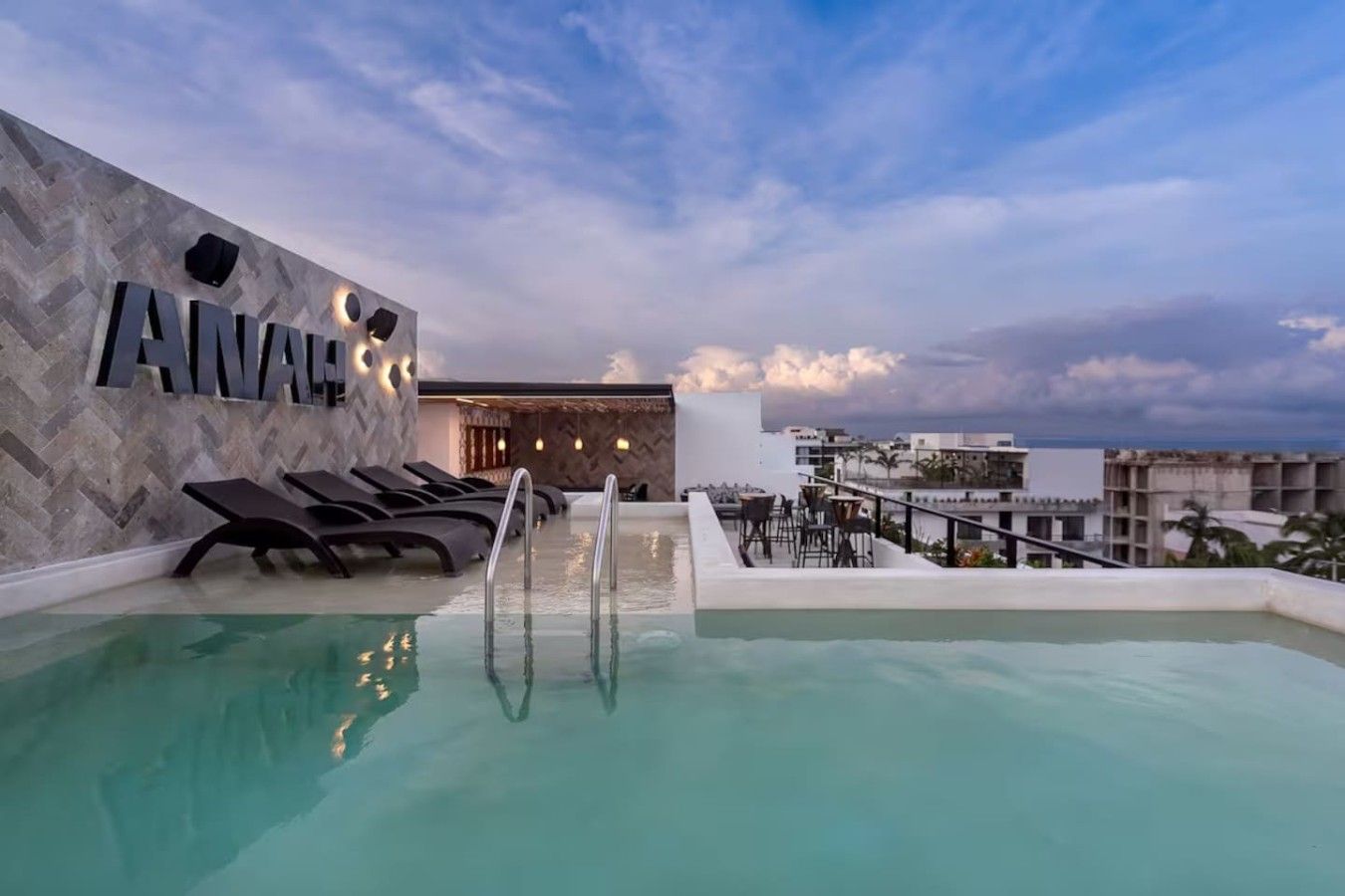 Zona de piscina en la azotea con sillones y un bar.