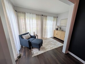 Ein modernes Wohnzimmer mit einer Couch, einem kleinen Beistelltisch, einem Schrank und einem großen Fenster mit leichtem Vorhang.
