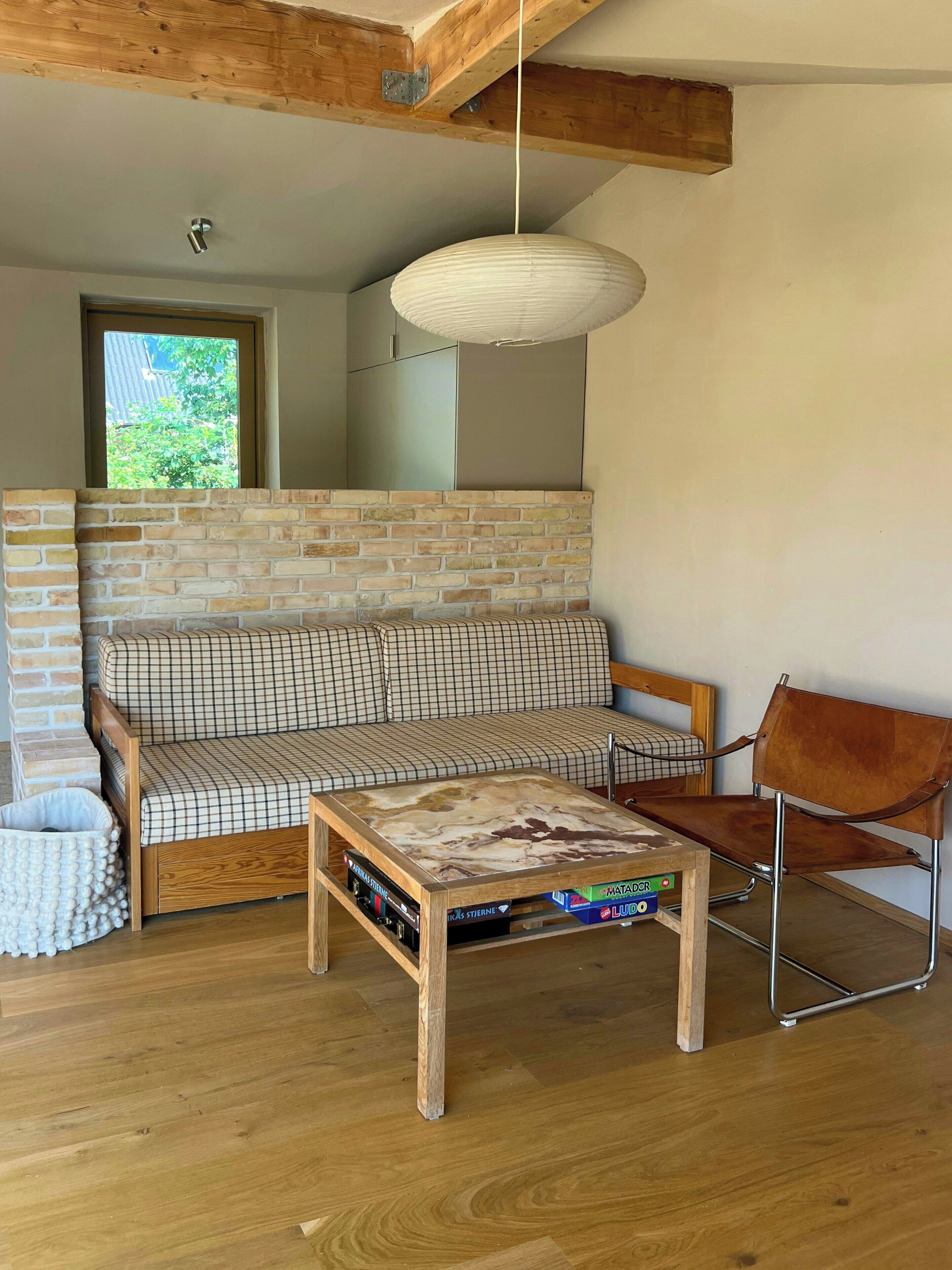 A modern living room with a brick wall, a sofa, a coffee table, a chair, and a hanging light fixture.