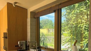 Een moderne keuken met houten kasten, een ingebouwde oven, een koffiezetapparaat, een spoelbak en een raam met uitzicht op groen.