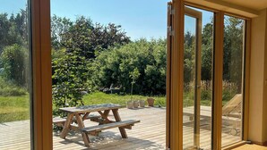Een houten terras met een picknicktafel, grote glazen deuren die uitkomen op een tuin, en een helder uitzicht op de omgeving.