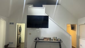 Una escalera con un televisor de pantalla plana montado encima, una consola con fotografías enmarcadas y un cuarto de lavado con lavadora y secadora.