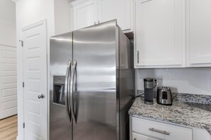 A stainless steel refrigerator, a coffee maker, and a toaster on a granite countertop in a kitchen with white cabinets. - 🐾 Lost Bay Townhome 4239 | Dog Friendly | New Build + Heart of Orange Beach (Orange Beach)