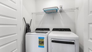 Una lavanderia con due lavatrici e asciugatrici a carica frontale, uno scaffale metallico sopra e una porta a sinistra.
