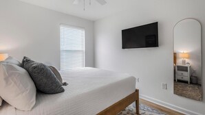 Una camera da letto con un letto, una ventola a soffitto, una TV, uno specchio e una finestra con persiane.