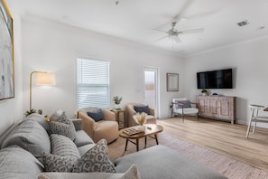 Ein modernes Wohnzimmer mit Sofa, Sesseln, Couchtisch, Fernseher und Deckenventilator.