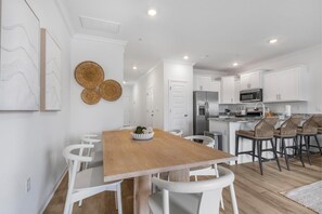 A modern kitchen with white cabinets, a wooden dining table, and white chairs. - 🐾 Lost Bay Townhome 4239 | Dog Friendly | New Build + Heart of Orange Beach (Orange Beach)