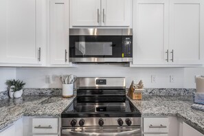 A kitchen with white cabinets, a stainless steel microwave, and a gas stove. - 🐾 Lost Bay Townhome 4239 | Dog Friendly | New Build + Heart of Orange Beach (Orange Beach)