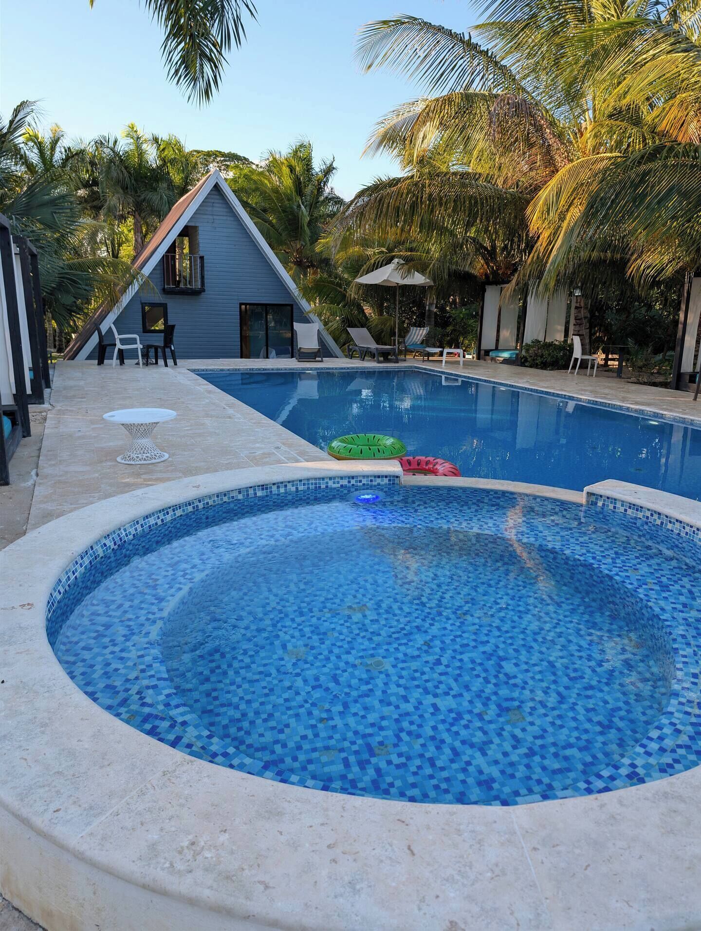 En pool med kakel runt kanten, omgiven av solstolar och ett litet bord.