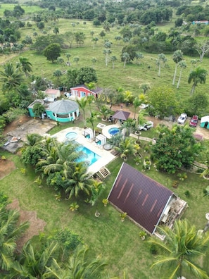 Zona residencial con piscina, una casa de techo rojo y vegetación circundante.