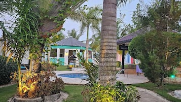 A garden with palm trees, a pool, and a building with a green roof.