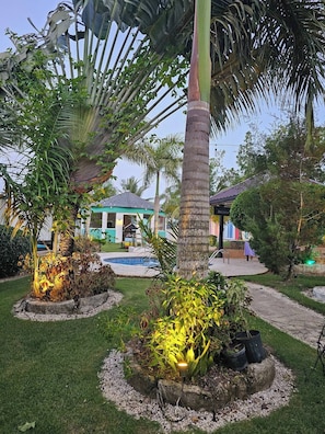 Un jardín con palmeras, una piscina y un edificio con techo verde.