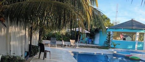 Una piscina con solárium azulejado, palmeras y sillones de descanso.