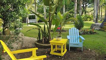 A garden with a yellow Adirondack chair, a small yellow table, and a blue Adirondack chair.