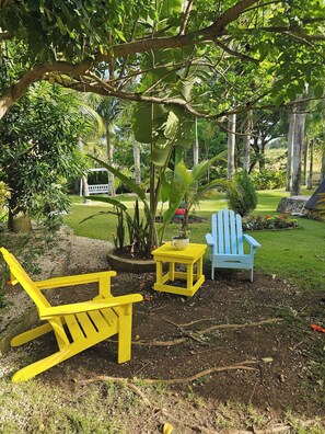 Un jardín con una silla Adirondack amarilla, una pequeña mesa amarilla y una silla Adirondack azul.