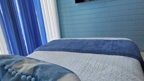 A bedroom with a bed, curtains, and a mounted television. - Cabaña Elian (Higüey)