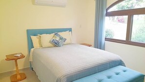 A bedroom with a bed, a bedside table, a window with curtains, and an air conditioning unit. - Villa and Casita (Tronadora)