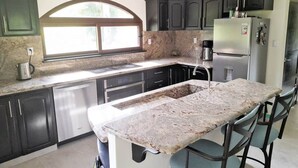 A kitchen with dark cabinets, a stainless steel refrigerator, a granite countertop, and a window above the sink. - Villa and Casita (Tronadora)