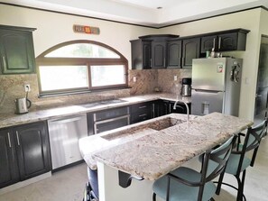 A kitchen with dark cabinets, a stainless steel refrigerator, a granite countertop, and a window above the sink. - Villa and Casita (Tronadora)
