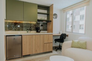 A compact kitchen with a built-in dishwasher, a coffee machine, and a clock on the wall.