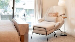 A hotel room with a bed, a chair, a lamp, and a view of the outdoors. - Luxury Condo E1 + Hot tub at Wapato Point Chelan (Manson)