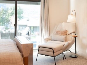 A hotel room with a bed, a chair, a lamp, and a view of the outdoors. - Luxury Condo E1 + Hot tub at Wapato Point Chelan (Manson)