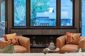 A room with a fireplace, two leather armchairs, and a view through large windows. - Luxury Condo E1 + Hot tub at Wapato Point Chelan (Manson)