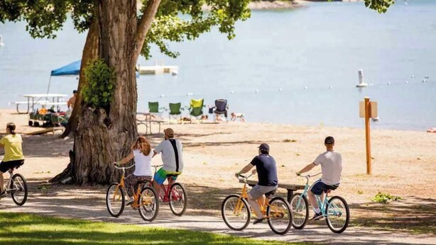 A group of people riding bicycles along a path by a lake with a picnic table and chairs in the background. - Luxury Condo E1 + Hot tub at Wapato Point Chelan (Manson)